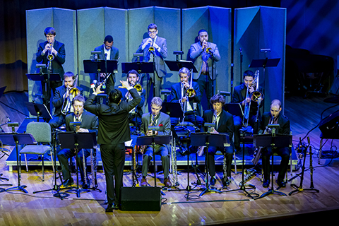 A director gestures with his hands at an orchestra as they perform.